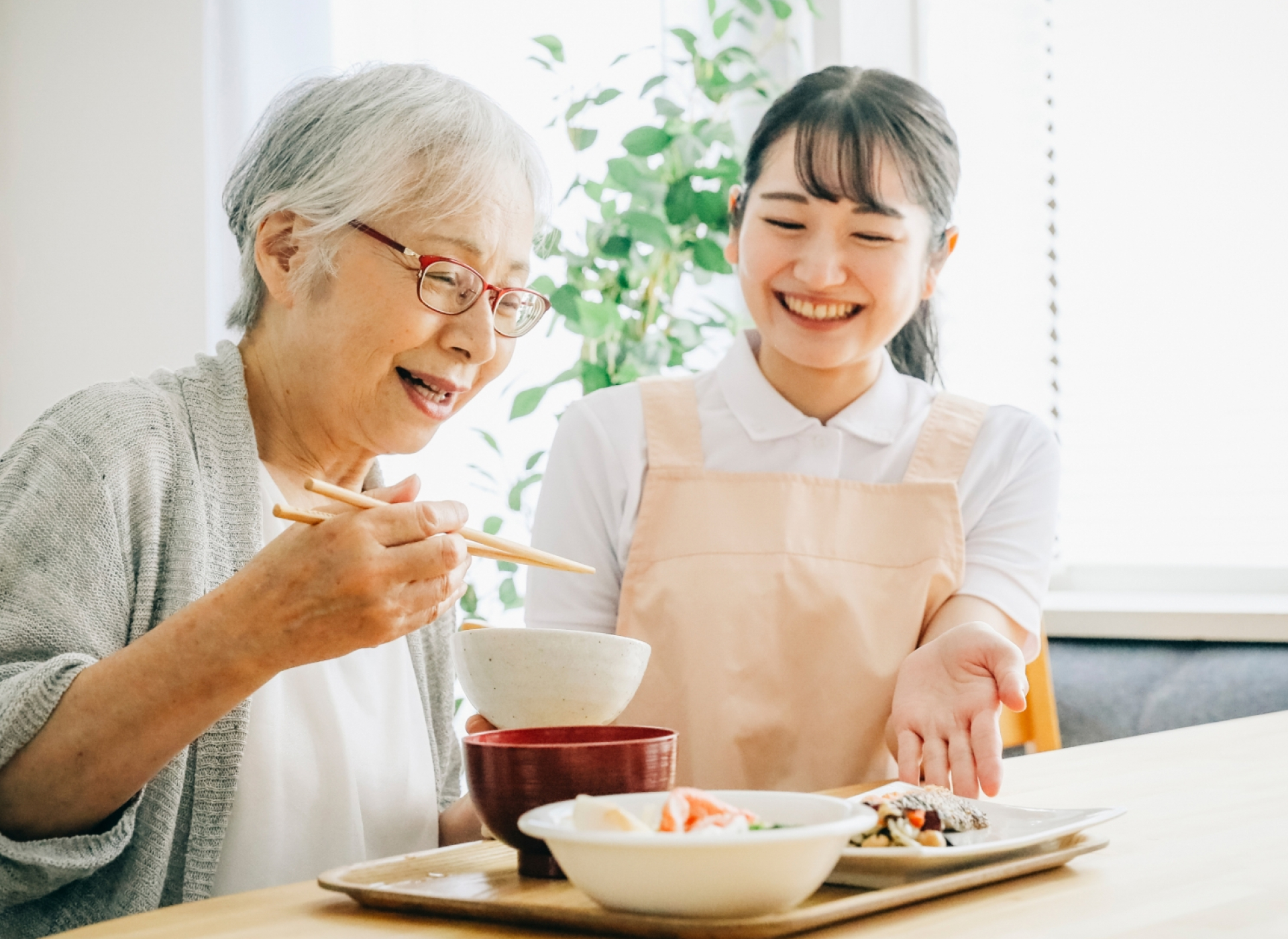 食事をする高齢者女性と施設員女性の写真