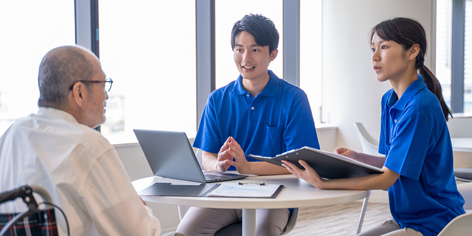 話し合いをする男女と車椅子に乗る高齢男性の写真